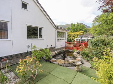 A garden area with a small pond surrounded by rocks and plants beside a white house at Haddef Penmaenmawr in Penmaenmawr