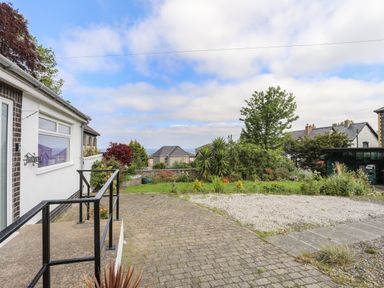 An outdoor area with a paved path gravel section and garden with bushes and trees near houses at Haddef Penmaenmawr in Penmaenmawr