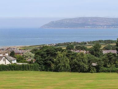 A grassy field with trees and houses near a coastline with a large hill in the background at Haddef Penmaenmawr in Penmaenmawr