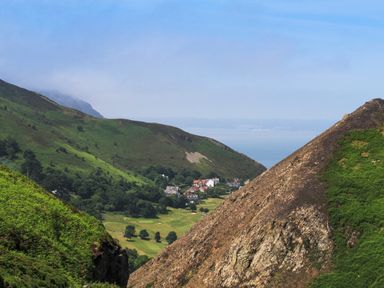 A valley with green hills trees houses and a view of the sea at Haddef Penmaenmawr in Penmaenmawr