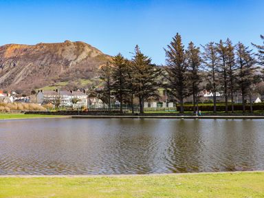 A pond with trees and houses with a mountain in the background at Haddef Penmaenmawr in Penmaenmawr