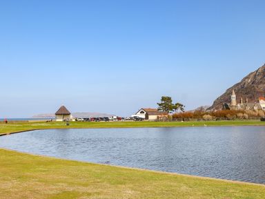 A pond with grass around it and buildings in the background at Haddef Penmaenmawr in Penmaenmawr