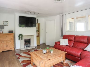 A living room with a red sofa wooden coffee table fireplace and a wall-mounted TV at Haddef Penmaenmawr in Penmaenmawr