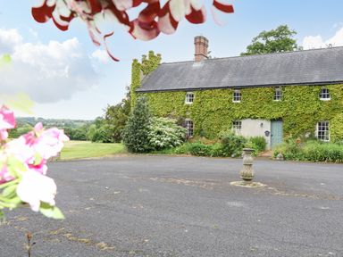 A courtyard with a stone pedestal in front of a building covered with ivy at Scarvagh House in Scarva near Loughbrickland