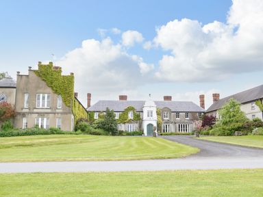 A large historic house with ivy on walls surrounded by green lawn and a driveway at Scarvagh House in Scarva near Loughbrickland