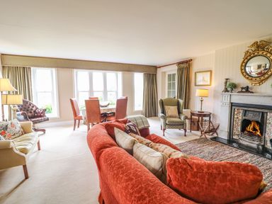 A living room with a red sofa a green armchair a dining table with chairs a fireplace with a fire and a round golden mirror above it at Scarvagh House Scarva near Loughbrickland