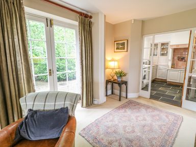 A room with a leather chair and blanket next to glass doors with curtains and a small table with lamp and plant by a doorway to a kitchen at Scarvagh House Scarva near Loughbrickland