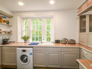 A kitchen with a washing machine under counters and a window above the sink with plants and kitchen appliances at Scarvagh House Scarva near Loughbrickland