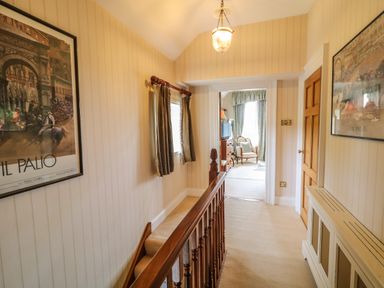 A hallway with framed pictures on walls a wooden banister and a doorway leading to a room with a chair at Scarvagh House in Scarva near Loughbrickland
