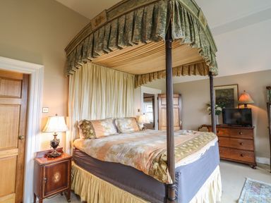 A bedroom with a four-poster bed bedside table with lamp wooden dresser with TV and a painting on the wall at Scarvagh House in Scarva near Loughbrickland