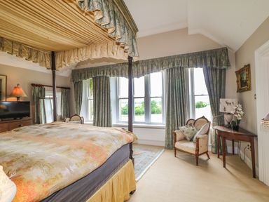 A bedroom with a four-poster bed a television an armchair and windows with long curtains at Scarvagh House Scarva near Loughbrickland