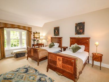 A bedroom with two wooden single beds a patterned rug a window with curtains and a dressing table with flowers at Scarvagh House Scarva near Loughbrickland