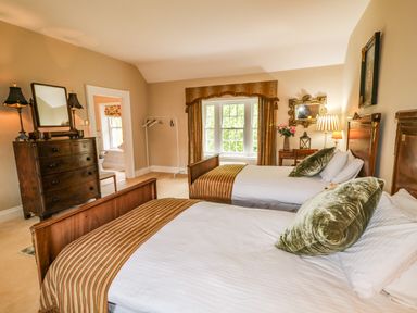 A bedroom with two single beds a wooden dresser a window with curtains and a small table with a lamp and flowers at Scarvagh House Scarva near Loughbrickland