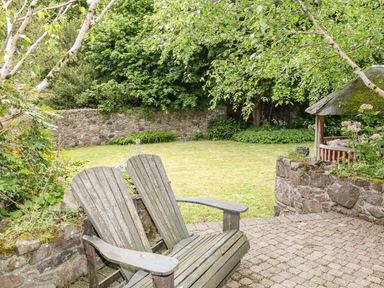 A garden with two wooden chairs on a stone patio and a stone wall with trees and grass at Scarvagh House Scarva near Loughbrickland