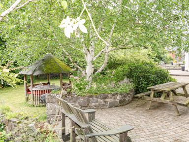 A garden with wooden bench and picnic table near a stone planter and a gazebo at Scarvagh House Scarva near Loughbrickland