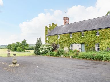 A stone building covered in ivy with a paved driveway and garden in a rural area at Scarvagh House Scarva near Loughbrickland