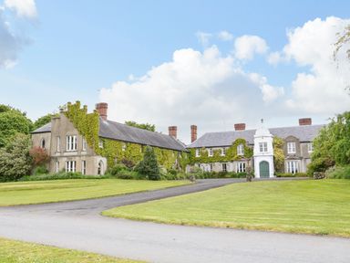 A large estate house with ivy on the walls and multiple chimneys surrounded by lawn at Scarvagh House in Scarva near Loughbrickland