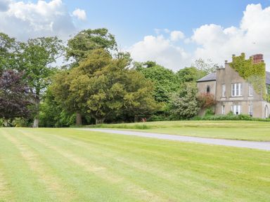 A large lawn with trees and shrubs surrounding a multi-story house partially covered with ivy at Scarvagh House Scarva near Loughbrickland