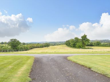 A paved driveway leading to a road with green grassy fields and trees in the background at Scarvagh House Scarva near Loughbrickland