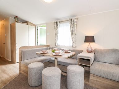 A dining area with a table set with bowls and glasses surrounded by upholstered bench seating and stools with a lamp on a side shelf by Herdwick Cabin in Troutbeck 68 White Cross Bay Holiday Park near Windermere