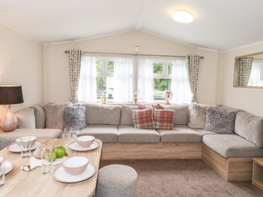 A living room with a grey sectional sofa and dining table set with bowls and glasses at Herdwick Cabin in Troutbeck 68 White Cross Bay Holiday Park near Windermere