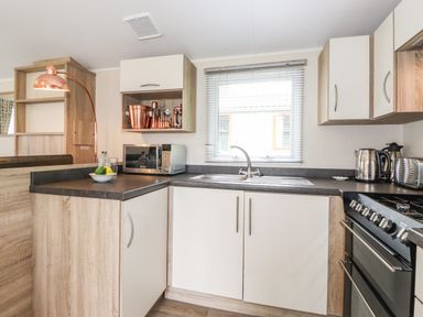 A kitchen with a stove sink microwave kettle and copper utensils at Herdwick Cabin Troutbeck 68 White Cross Bay Holiday Park near Windermere