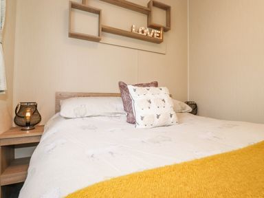 A bed with sheep patterned bedding and pillows a wooden shelf with a love sign and two bedside tables with lamps at Herdwick Cabin in Troutbeck 68 White Cross Bay Holiday Park near Windermere