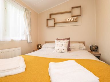 A bedroom with a bed a yellow blanket pillows and towels on the bed at Herdwick Cabin Troutbeck 68 White Cross Bay Holiday Park near Windermere