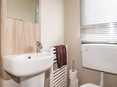 A bathroom with a sink, mirror, towel on a radiator, toilet, and window blinds at Herdwick Cabin in Troutbeck 68 White Cross Bay Holiday Park near Windermere
