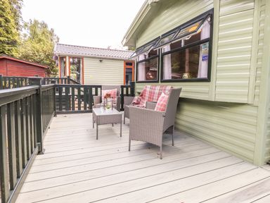 An outdoor deck with wicker chairs and a table outside a green cabin at Herdwick Cabin in Troutbeck 68 White Cross Bay Holiday Park near Windermere