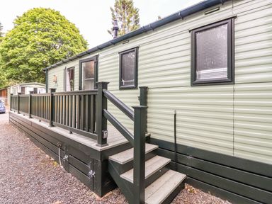 A light green mobile home with black railings and stairs next to gravel path at Herdwick Cabin Troutbeck 68 White Cross Bay Holiday Park near Windermere