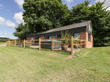 A single-story brick and wood building with a fenced patio and potted plants surrounded by grass and trees at The Old Kennels in Harcombe near Sidford