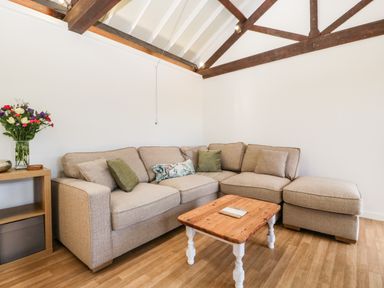 A living room with a beige sectional sofa a wooden coffee table and flowers on a side table at The Old Kennels in Harcombe near Sidford