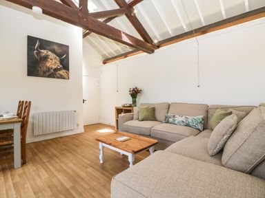 A living room with a beige sofa a wooden coffee table flowers on a side table and a dining table with chairs at The Old Kennels in Harcombe near Sidford