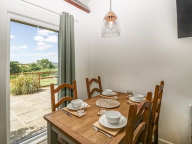 A dining area with a wooden table set for four and a glass door showing an outdoor patio at The Old Kennels in Harcombe near Sidford