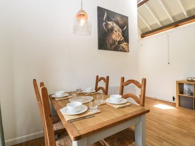 A dining room with wooden table and chairs set with white dishes and glassware and a painting of a bull on the wall at The Old Kennels in Harcombe near Sidford