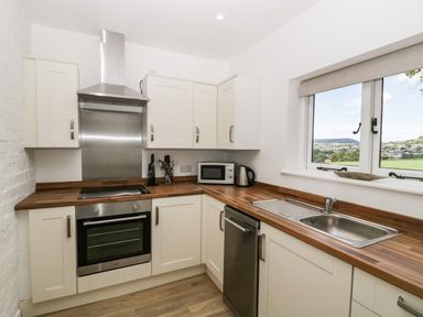 A kitchen with white cabinets wooden countertops a stainless steel oven and sink and a window showing outside view at The Old Kennels in Harcombe near Sidford