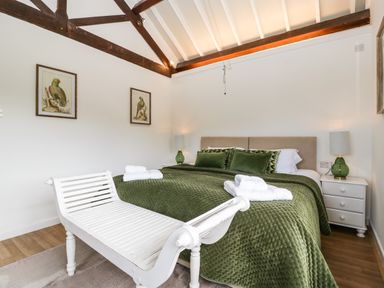 A bedroom with a double bed green bedspread green pillows white bench and bedside tables with lamps at The Old Kennels in Harcombe near Sidford