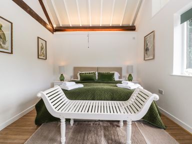 A bedroom with a green bedspread green pillows white bench and two bedside tables with lamps at The Old Kennels in Harcombe near Sidford