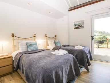 A bedroom with two single beds blue pillows and gray covers next to a glass door showing an outdoor view at The Old Kennels in Harcombe near Sidford