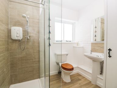 A bathroom with a shower, toilet with wooden seat, sink, and window at The Old Kennels in Harcombe near Sidford