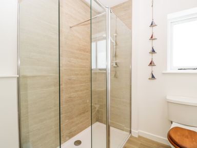A bathroom with a glass-enclosed shower and a toilet with a wooden seat near a window at The Old Kennels in Harcombe near Sidford