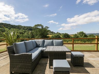 An outdoor patio with wicker furniture and cushions overlooking a grassy landscape at The Old Kennels Harcombe near Sidford