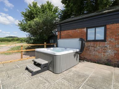 An outdoor hot tub with steps on a stone patio next to a brick building at The Old Kennels in Harcombe near Sidford