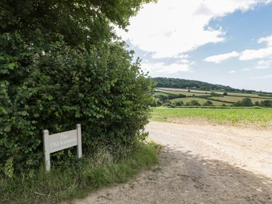 A dirt road next to a bush with a sign reading The Old Kennels with fields and hills in the background at The Old Kennels in Harcombe near Sidford