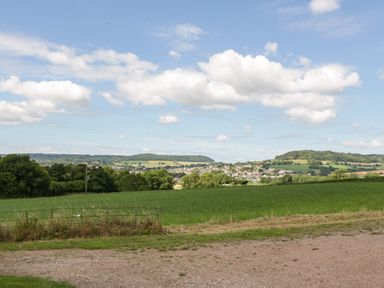 A rural landscape with green fields trees and hills under a blue sky at The Old Kennels in Harcombe near Sidford