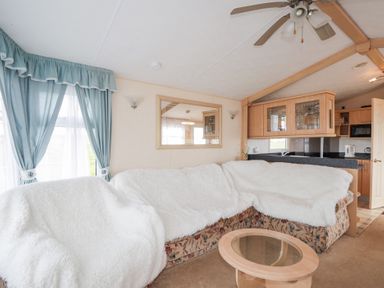 A living room with a sectional sofa covered with white throws a glass coffee table a ceiling fan and blue curtains at The Cabin in Occumster near Lybster