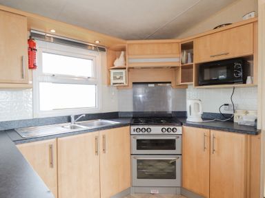A kitchen with wooden cabinets a double sink a stove microwave and kettle at The Cabin in Occumster near Lybster