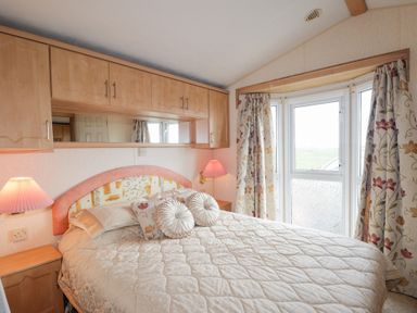 A bedroom with a bed with pillows bedside tables with lamps and a window with floral curtains at The Cabin in Occumster near Lybster