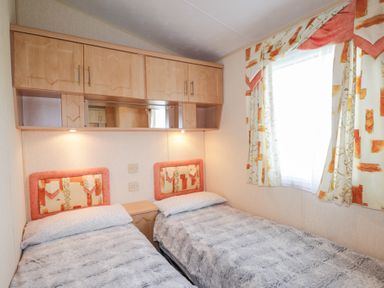 A bedroom with two single beds side by side under wooden cabinets and a window with patterned curtains at The Cabin in Occumster near Lybster